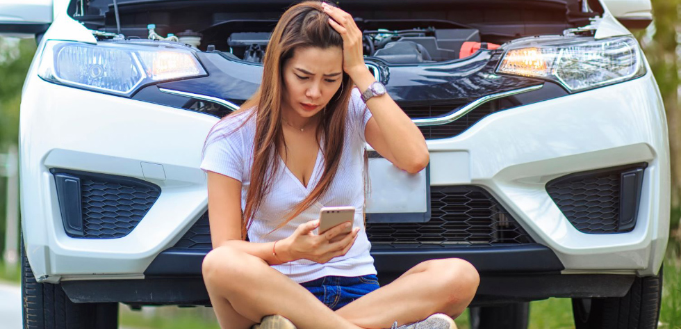 Woman sitting on pavement with car that has a dead battery